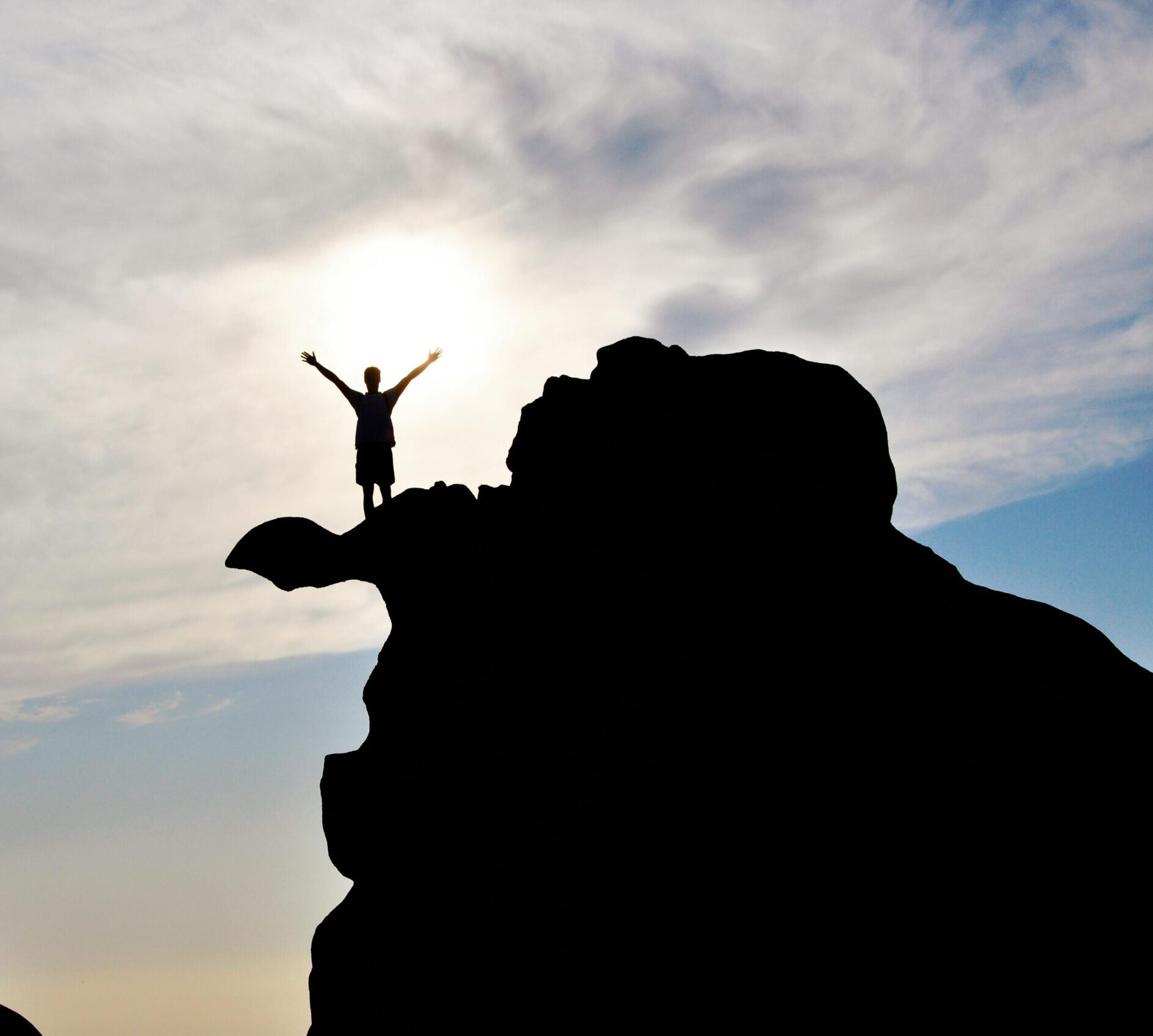 Silhouette of a person celebrating on a mountain peak against a dramatic sky, symbolizing freedom and success.